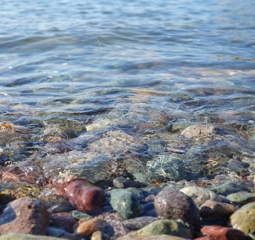 Crystal clear water gently lapping colourful pebbles depicting a calm environment for wellbeing