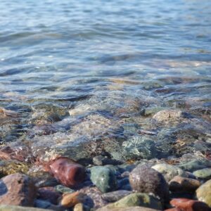 Crystal clear water gently lapping colourful pebbles depicting a calm environment for wellbeing